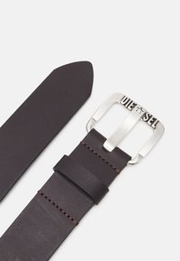 Cinturón de cuero marrón oscuro con una superficie elegante y suave. Cuenta con una hebilla rectangular plateada con la inscripción "DIESEL" y detalles de costura en marrón.