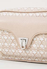 Borsa a mano in pelle beige con una superficie texturizzata, caratterizzata da un motivo geometrico e una chiusura in argento. Il design include sottili dettagli di cucitura.
