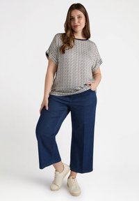 Lätt mönstrad topp med korta ärmar i kräm och marinblå, kombinerad med mörkblå vida jeans och beiga sneakers.