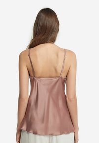 Satin cami i mjuk rosa, med tunna justerbara axelremmar och en flödande design som sveper försiktigt över ryggen och axlarna.