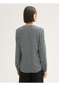 Camisa de manga larga con estampado en blanco y negro, que presenta un diseño de pata de gallo, cuello redondo y puños elásticos. Textura de tela suave.