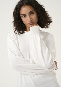 Witte trui met lange, gepofte mouwen met een textuur van diamantpatroon, versierd met kleine, parelachtige accenten. Zacht breimateriaal.