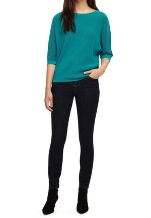 Tiefblaues geripptes Strickpullover mit weiter Ausschnittform und lockerer Passform, kombiniert mit dunklen Skinny-Jeans und Ankle Boots. Weiche Textur, lässiges Design.