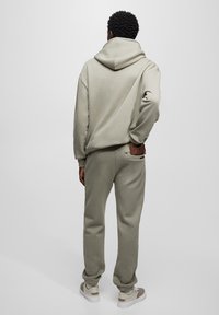 Sudadera con capucha de color gris claro con una capucha grande, combinada con pantalones deportivos grises a juego con un bolsillo trasero. Textura suave, ajuste relajado y puños acanalados.