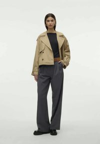 Bež värveldatud kahepoolne jakk musta särk üle, koos vaba hallide pükstega ja pruuni vöödiga. Mustad kingad täiendavad komplekti.