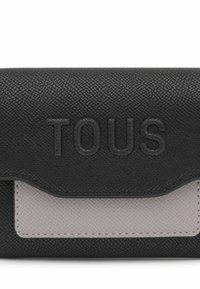Black pebbled leather wallet with a light gray textured panel; embossed "TOUS" logo on the front; flap closure design.