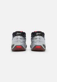 Baskets de sport avec une tige noire et argentée, présentant un design élégant, une semelle en caoutchouc et des accents rouges sur le talon et la semelle extérieure.