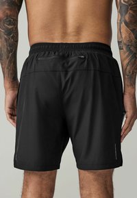 Black athletic shorts with an elastic waistband, featuring a smooth texture, two rear pockets, and a stitched hem at the legs.