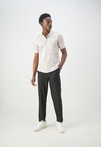Light-colored short-sleeve shirt with palm tree pattern, paired with black ribbed trousers and white sneakers. Casual, relaxed fit.