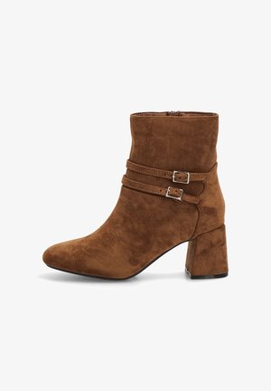 Botín de ante marrón con punta afilada, dos correas decorativas con hebillas y un tacón grueso de bloque. Textura suave con detalles de costura.