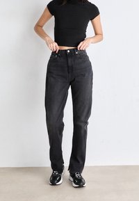 Black ribbed crop top paired with high-waisted dark denim jeans. Model wears black and white sneakers. Smooth texture, classic design.