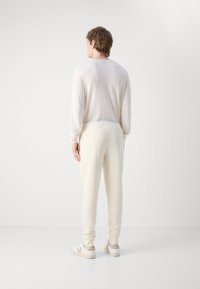 Lichtromkleurige, lange mouwtop en bijpassende joggerbroeken gemaakt van zachte stof, met een elastische tailleband en aansluitende boorden. Witte sneakers met beige accenten.