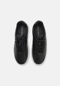 Black leather sneakers with smooth texture, round toe, lace-up design, and white rubber sole. Features "Calvin Klein" branding inside.