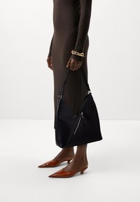 Svart läderaxelväska med en unik V-form, med en ficka med dragkedja, tillsammans med en brun ribbad klänning och spetsiga bruna mules.