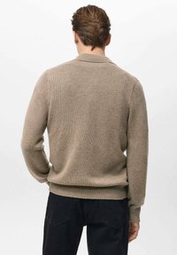 Beige gebreide trui met een ronde hals en geribbelde boorden en zoom. De stof is zacht en gestructureerd, met een eenvoudig, klassiek ontwerp.