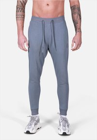 Pantaloni jogger grigi con una vestibilità affusolata, vita elasticizzata, lacci e polsini a coste. Presenta un logo sottile sulla coscia.