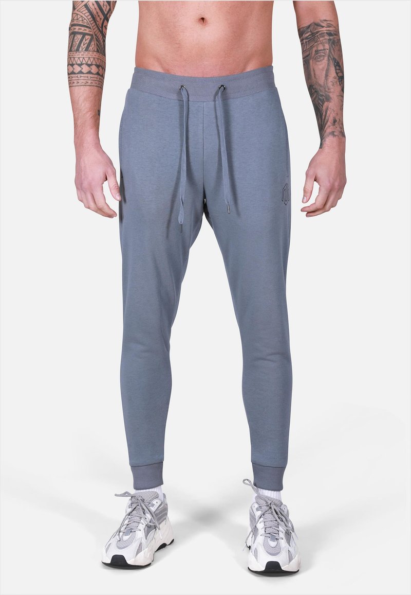 Pantaloni jogger grigi con una vestibilità affusolata, vita elasticizzata, lacci e polsini a coste. Presenta un logo sottile sulla coscia.