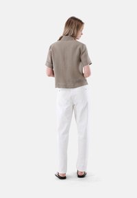 Top beige a maniche corte, morbido e con orlo dritto; abbinato a pantaloni bianchi a vita alta e sandali bassi.