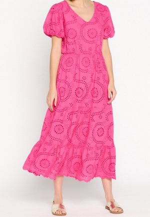 Robe midi rose vif avec manches bouffantes, broderie anglaise, taille froncée et jupe à volants portée avec des sandales plates beiges.