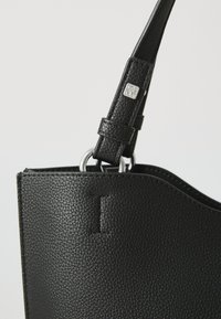 Black leather handbag with a pebbled texture, featuring silver hardware and a circular ring attachment on a slim strap.