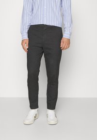 Ciemnoszare spodnie o dopasowanym kroju, wykonane z teksturowanej tkaniny. Posiadają zapięcie na guziki i boczne kieszenie, zestawione z białymi trampkami.