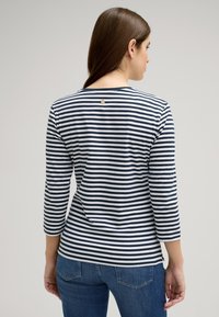 Maglietta a righe blu navy e bianca con maniche lunghe, scollatura rotonda e un piccolo dettaglio in metallo nella parte superiore della schiena. Tessuto morbido con vestibilità comoda.
