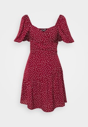 Robe rouge à pois blancs avec manches bouffantes courtes, corsage ajusté et jupe évasée. Confectionnée dans un tissu léger à texture lisse.