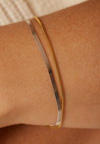 Zilveren en gouden bangle armbanden met een slank, dun ontwerp dat op een gebruinde pols rust; gladde, gepolijste afwerking en minimale details.
