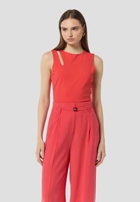 Czerwona bezrękawnik z wycięciem na ramieniu, zestawiony z różowymi spodniami o wysokim stanie i szerokich nogawkach. Gładki, teksturowany materiał.