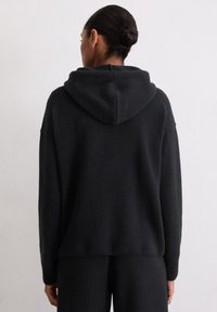 Czarny, dziergany sweter z kapturem, wykończony prążkowanym dołem i mankietami. Miękka faktura, luźny krój, prosty design bez ozdób.