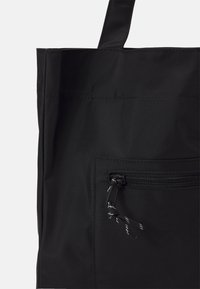 Borsa a spalla nera realizzata in tessuto resistente, dotata di una tasca con zip e un'opportuna linguetta di apertura, e spallacci piatti e robusti.