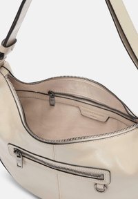 Kremowa skórzana torebka na ramię z zamkiem błyskawicznym w głównym komorze, kieszenią wewnętrzną i srebrnymi elementami. Gładka faktura z kontrastującymi detalami w szwie.