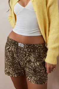 Brown leopard print shorts with elastic waistband, paired with a white tank top and a yellow fuzzy cardigan. Visible brand label on shorts.