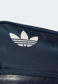Tamsiai mėlynas tekstūruotas maišelis su baltu Adidas trijų lapų logotipu ir trimis horizontaliomis juostelėmis apačioje. Tvirtas medžiagos pasirinkimas ir be siūlių dizainas.