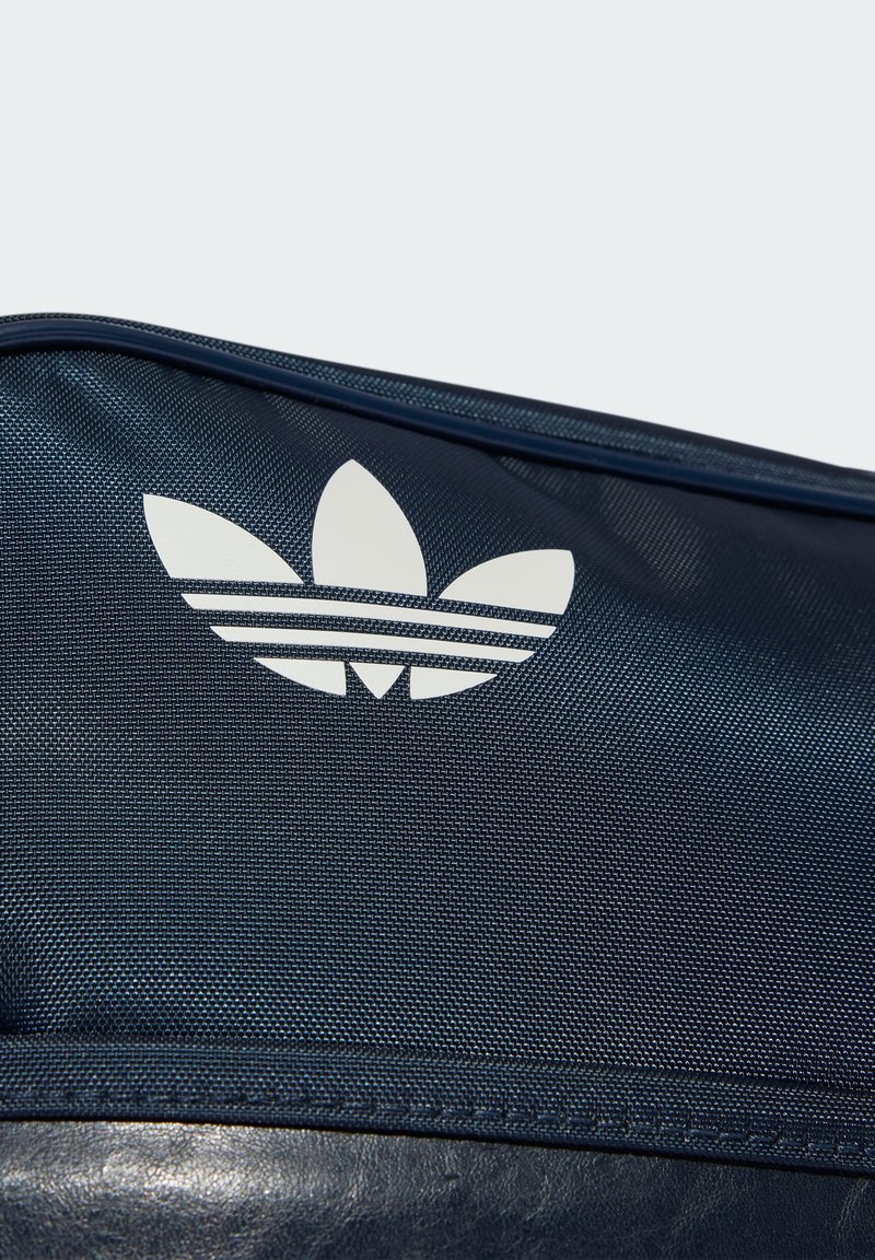Navyblaue, strukturierte Tasche mit einem weißen Adidas-Drei-Blätter-Logo und drei horizontalen Streifen darunter. Robustes Material und nahtloses Design.