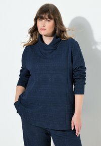 Pullover blu navy con collo a cascata, caratterizzato da motivi geometrici testurizzati, maniche lunghe e tasche laterali. Tessuto morbido e vestibilità rilassata.
