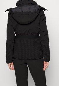 Black jacket with a textured knit fabric at the waist, smooth upper section, attached hood, and a belted design for a fitted silhouette.