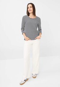 Gestreepte langemouwen top in zwart en wit, gecombineerd met wijde witte broeken en sneakers. Casual fit met zijzakken en een ronde halslijn.