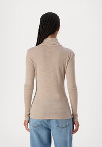 Beige langermet genser med rullekrage, tettsittende silhuett og myk tekstur; kombinert med lyseblå denimjeans.