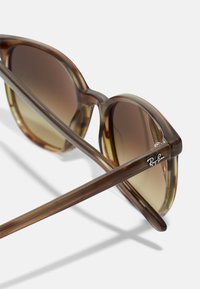 Ochelari de soare tortoiseshell maro cu lentile gradient. Ramă rotundă, brațe subțiri cu logo-ul Ray-Ban argintiu și finisaj lucios.
