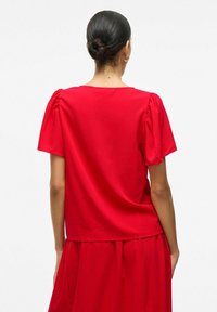 Czerwony top z krótkim rękawem z bufkami, okrągłym dekoltem i luźnym krojem, wykonany z lekkiego materiału o gładkiej fakturze.