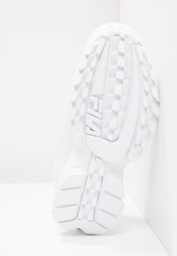 Suela de zapatilla blanca con patrón de agarre texturizado y logotipo en relieve. El material parece goma con perforaciones en el lateral para mayor transpirabilidad.