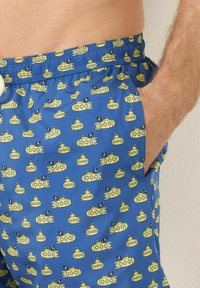 Shorts de bain bleus ornés d'un motif de sous-marins jaunes avec des drapeaux de pirate noirs. Fabriqués en tissu léger avec une taille élastique.