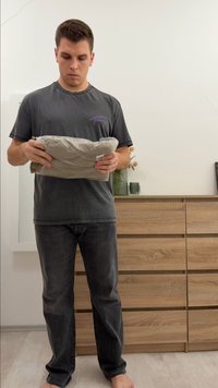 Folded textured blanket in a light beige color, held by a person. Neutral background with wooden dresser and decorative items visible.