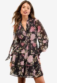 Rochie neagră cu flori roz și crem, cu mâneci lungi, bufante, fustă în straturi și talie elastică. Realizată dintr-un material ușor și translucid.