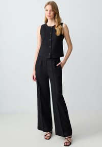 Completo in lino nero composto da un top cropped senza maniche con bottoni frontali e pantaloni a gamba larga con tasche laterali.