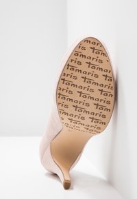 Chaussure à talon haut en daim rose blush avec un bout pointu et un talon fin. La semelle présente un motif répétitif du logo "Tamaris".