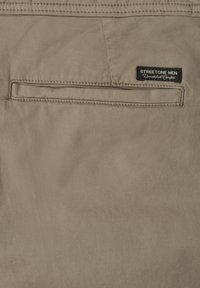 Tissu beige en gros plan montrant une poche passepoilée arrière et une étiquette noire mentionnant « Streetone Men Unmatched Comfort ».