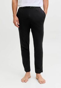 Černé slim-fit kalhoty s elastickým pasem, na kterém je bílý text s logem. Vyrobeny z měkké tkaniny, navrženy pro pohodlí a každodenní nošení.