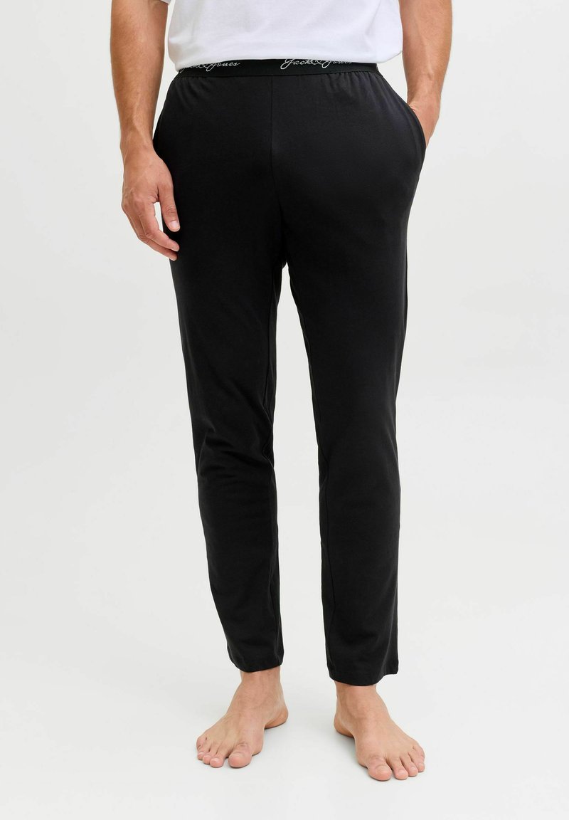 Černé slim-fit kalhoty s elastickým pasem, na kterém je bílý text s logem. Vyrobeny z měkké tkaniny, navrženy pro pohodlí a každodenní nošení.